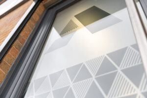 Storefront window with frosted geometric pattern of triangles and stripes on glass, brick wall visible in frame.