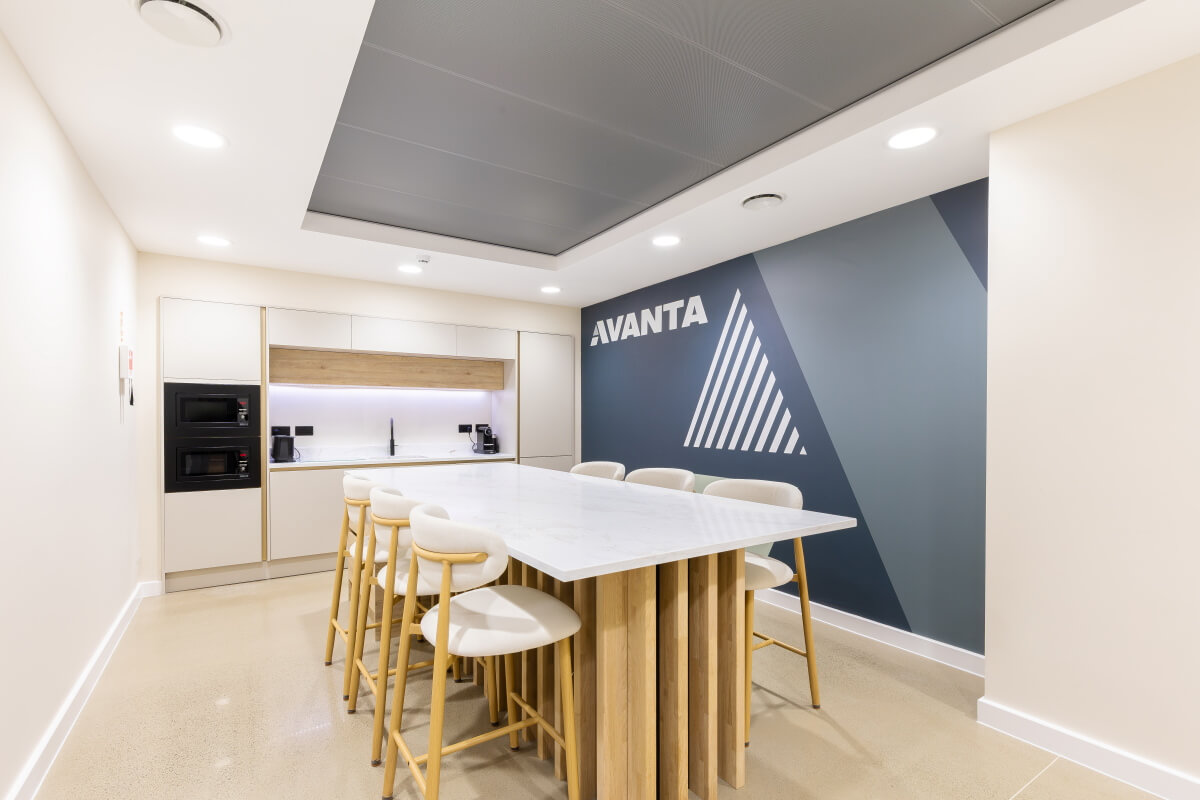 Modern kitchenette and coffee area with a long marble island and light wood stools, AVANTA wall mural in blue geometric design.