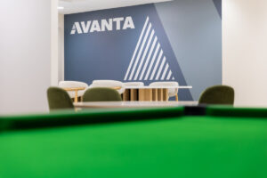 Branding wall in AVANTA office with a blue geometric mural, a white table and chairs, and a green pool table in the foreground.